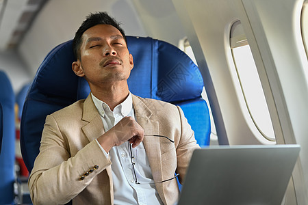 千年商务人士在飞机机舱坐着舒适的座位时 分心于计算机工作而离开电脑工作图片