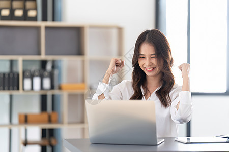 年轻的商业女青年在办公室的办公桌前享受快乐生意人女孩成功女性笔记本人士工作职业微笑商务图片