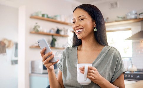 年轻的混血西班牙裔女性早上在家打电话喝咖啡 年轻女性在家里使用社交媒体或用手机发短信时微笑图片