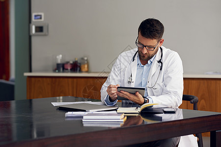 一个英俊的男医生坐在办公室里 在他的药片上工作 他把药片弄得一团糟图片