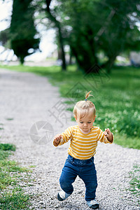 小女孩走在公园的碎石路上 看着她的脚下图片
