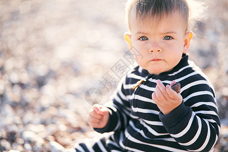 身穿条纹内裤的严重婴儿坐在一个石子海滩上 手里握着一块石子图片