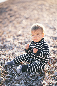 身穿条纹内裤的幼童坐在一个石子海滩上 手握拳头在前面图片