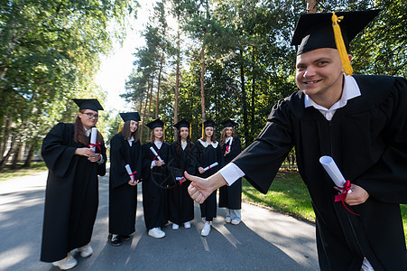 一群在户外的研究生 他们很快乐地从咖啡馆毕业的男毕业生身上伸出拇指图片