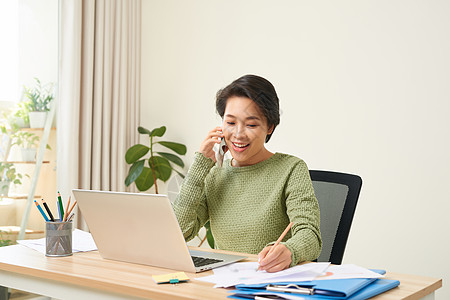 妇女在家里用笔记本电脑工作 同时通过电话交谈营销手机女士信息金融女性微笑技术单元办公室图片