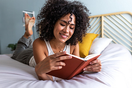 快乐的年轻多种族女人躺在床上 在家里看书放松一下 在床上图片