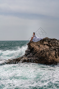 暴风雨中的一个女人坐在海面的一块石头上 穿着白色长裙 波浪冲向岩石 白喷雾上升太阳头发风暴海岸海浪旅行支撑冲浪碰撞海洋图片