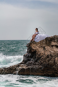 暴风雨中的一个女人坐在海面的一块石头上 穿着白色长裙 波浪冲向岩石 白喷雾上升海浪旅行风暴悬崖天空女士成人冲浪头发女性图片