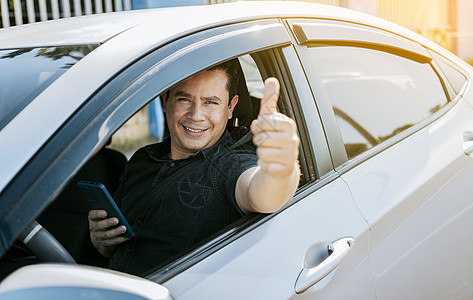 拿着手机的微笑司机竖起大拇指 司机拿着手机竖起大拇指 快乐的司机在路上竖起大拇指 安全驾驶理念图片