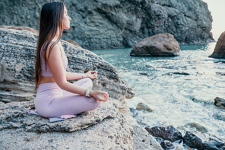 黑头发的年轻女子 穿着粉色紧身裤和上衣的健身教练在日落时分在海边的火山岩上做伸展运动和普拉提 女性健身瑜伽常规概念 健康的生活方图片