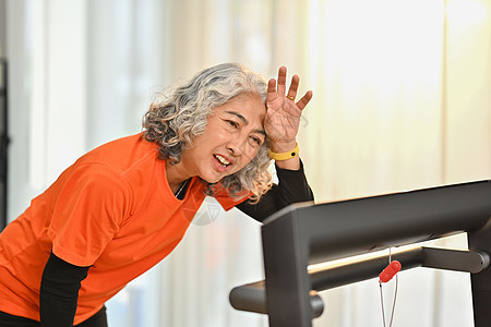 在室内跑步机上冲洗后 年长妇女疲劳地在前额擦汗 健康活跃的生活方式概念图片