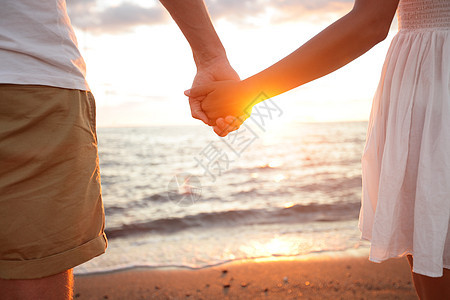夏天的情侣在海滩日落时握手图片