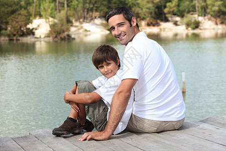 一个父亲和他的儿子坐在浮舟上 面对着一个湖图片