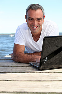 男人用笔记本电脑在木制码头上图片