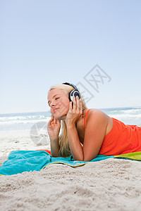 深思熟虑的年轻女子躺在沙滩上听音乐图片
