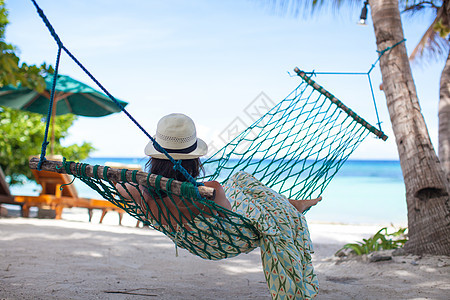 戴帽子的女人躺在吊床上 在海滩树影的阴影下图片