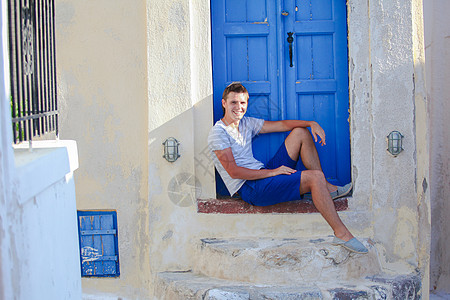 年轻人坐在希腊圣托里尼岛Emporio村旧蓝色门附近 农村 文化图片