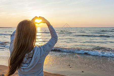 女孩在海滩上握着双手的心型 制作 水 女孩们图片