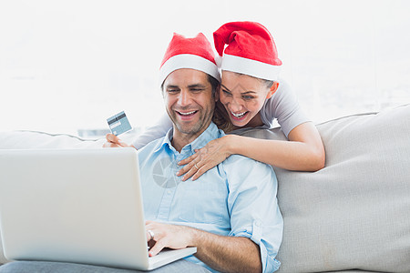 用笔记本电脑在网上购物的圣塔帽上微笑情侣 漂亮的图片