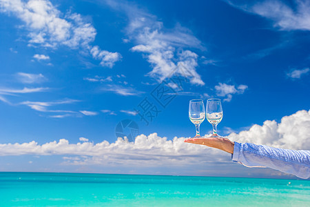 蓝色天空背景的雄手用两杯干净的眼镜 抓住 海洋图片