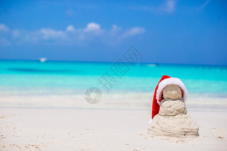 带圣诞帽的雪人在加勒比海白沙滩上 带红色圣塔帽子的小沙沙雪人 女孩 蓝色的背景