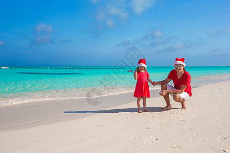 在奇异海滩的圣塔帽子 圣诞礼堂的小女孩和快乐爸爸 圣诞节 水图片