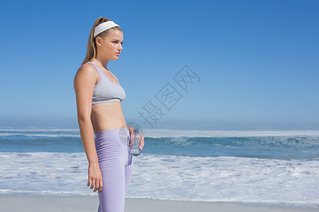 运动金发金发美女站在沙滩上 喝着水瓶子图片