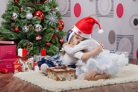 两个女孩在圣诞树旁边拥抱两个女孩 玩具 幸福背景图片