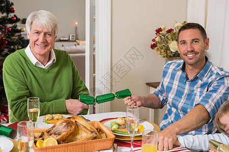 圣诞晚餐微笑的祖父和父亲拉着圣诞饼干来玩背景