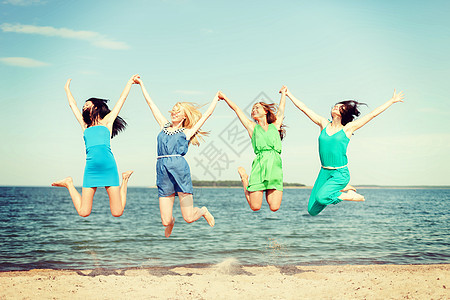 笑笑着的女孩在海滩上跳跃 海岸 公司 漂亮的 连衣裙图片