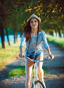 戴着帽子的可爱年轻女子在户外骑自行车 时尚图片