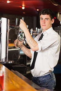 在啤酒喷洒器上拿着玻璃杯的酒吧管家肖像图片