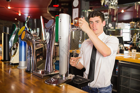 酒保拿着玻璃站在啤酒喷洒器前面的酒商图片