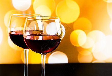 两杯红葡萄酒 在木桌上用两杯红酒 以金色布基灯光为背景图片