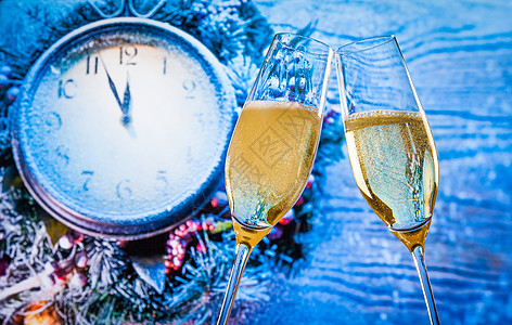午夜的新年或圣诞节 香槟长笛和金泡泡在蓝光和时钟上欢呼图片