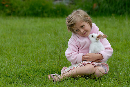 穿粉红色衣服的可爱小女孩在照顾小白兔 脸图片