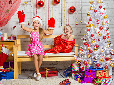 长凳上坐着一个戴着帽子和圣诞老人连指手套的女孩 另一个笑着从包里出来的女孩图片