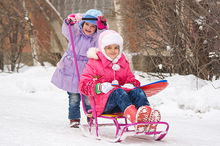 女孩在院子的雪橇上翻另一个女孩图片