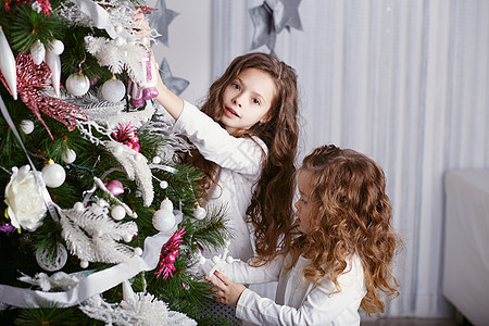 两个小姐妹 装饰圣诞树 配有玩具和球图片