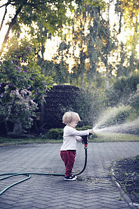 婴儿女婴在花园里用水管浇水 花朵 照顾花园 树木 植物图片