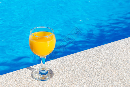 在游泳池边缘的玻璃杯上加橙汁图片