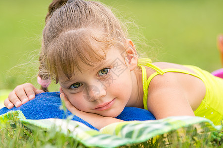 5岁女孩躺在绿色草地上的床上 触摸着框架的图样图片