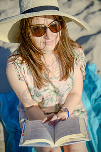 干发帽在海滩上放松 阅读一本书的褐发美女肖像 闲暇背景
