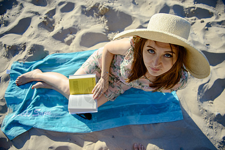 干发帽在海滩上放松 阅读一本书的褐发美女肖像 水背景