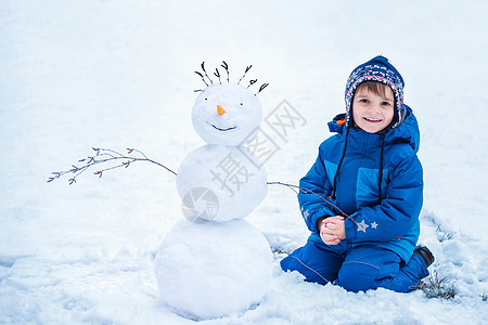 坐在微笑的雪人旁边的小男孩图片