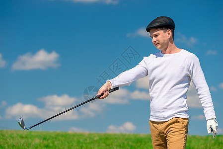 绿色竞技场上身着帽子和高尔夫俱乐部的青年高尔夫球手图片
