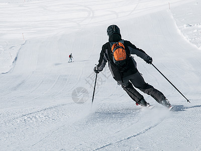 在滑雪坡上滑雪的黑色下山滑雪中的滑雪者 从后面查看图片