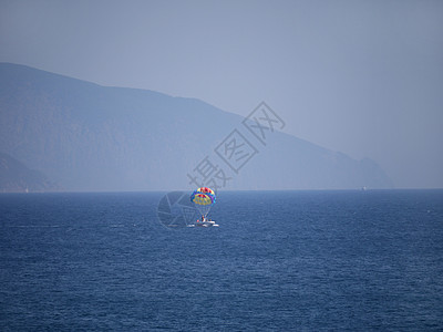 乘游船与旅游者渡渡过蓝海和远处高岩山的度假船只图片