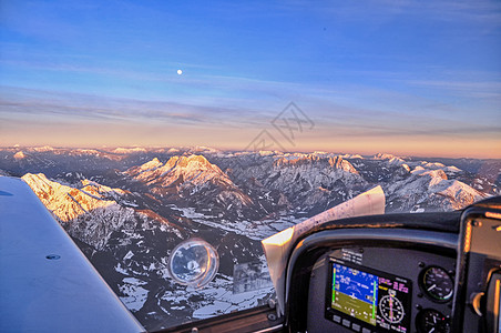 日落时在奥地利上空阿尔卑斯山顶上空飞行的轻型运动飞机 顶峰 森林背景