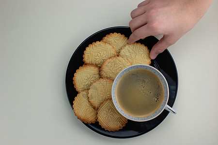 黑色盘子和黑咖啡杯上自制的短面包 小孩手拿着一块饼干 顶级风景 肉桂 烤的图片